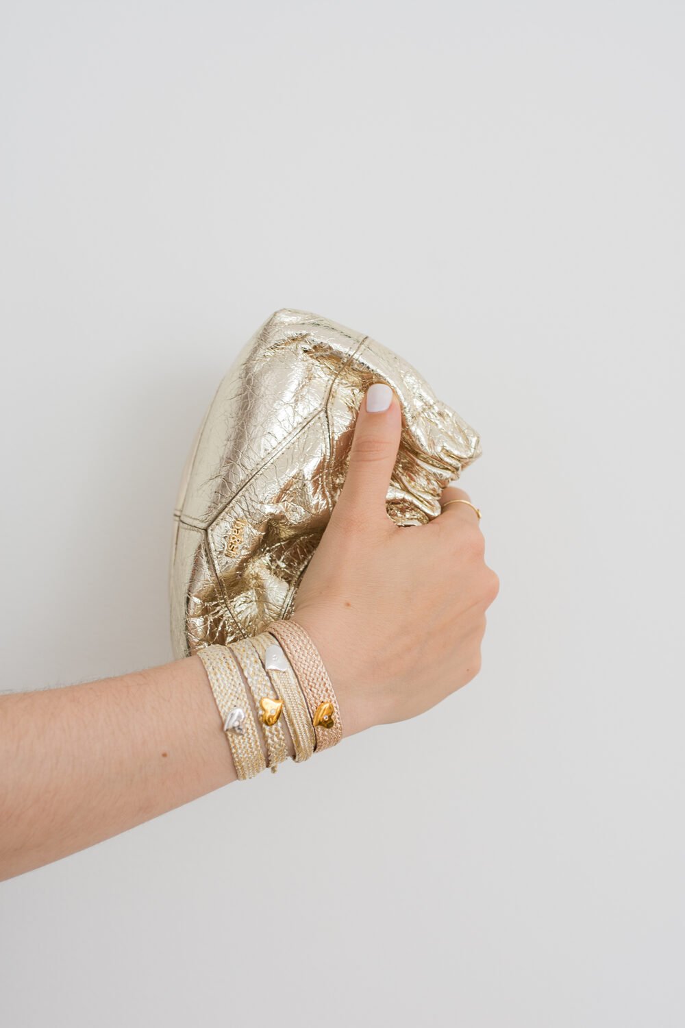 Mano con pulseras apiladas sujetando un bolso dorado