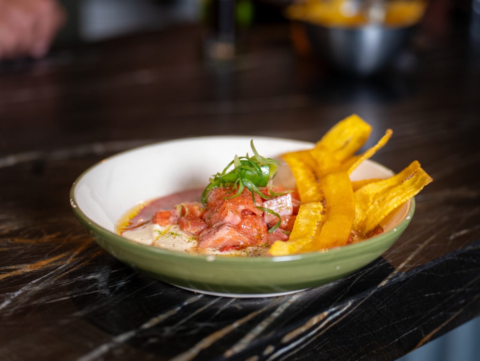 Cebiche con plátano frito servido en plato verde sobre mármol oscuro
